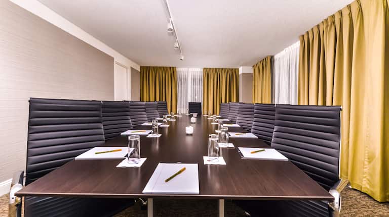 Long Boardroom Table in Private Meeting Room With Seating for 12 and View Toward Head of Table Surrounded by Windows with Yellow Drapes