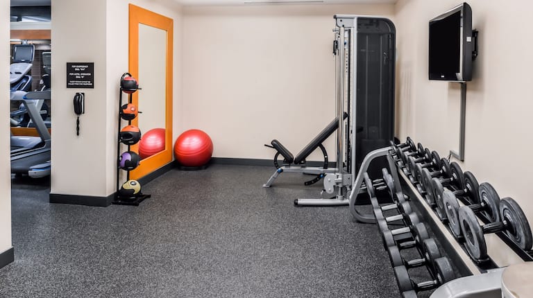 Fitness Center With Weight Balls, Full Length Mirror, Red Exercise Ball, Weight Bench, TV, and Free Weights With Doorway Open to Cardio Equipment