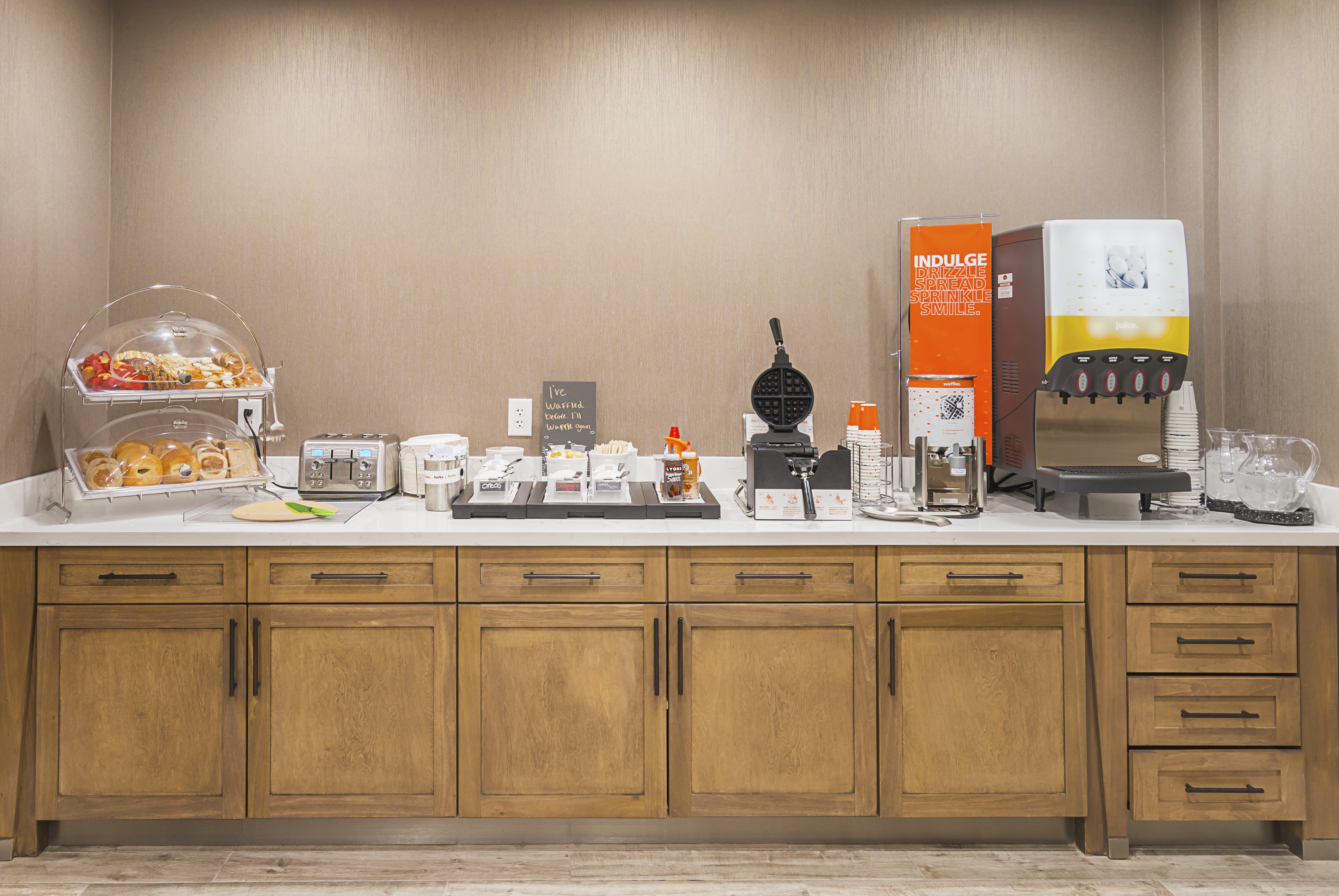 Breakfast buffet counter and cabinetry
  with juice machine, pastries, and waffle machine with a variety of topping
  options
