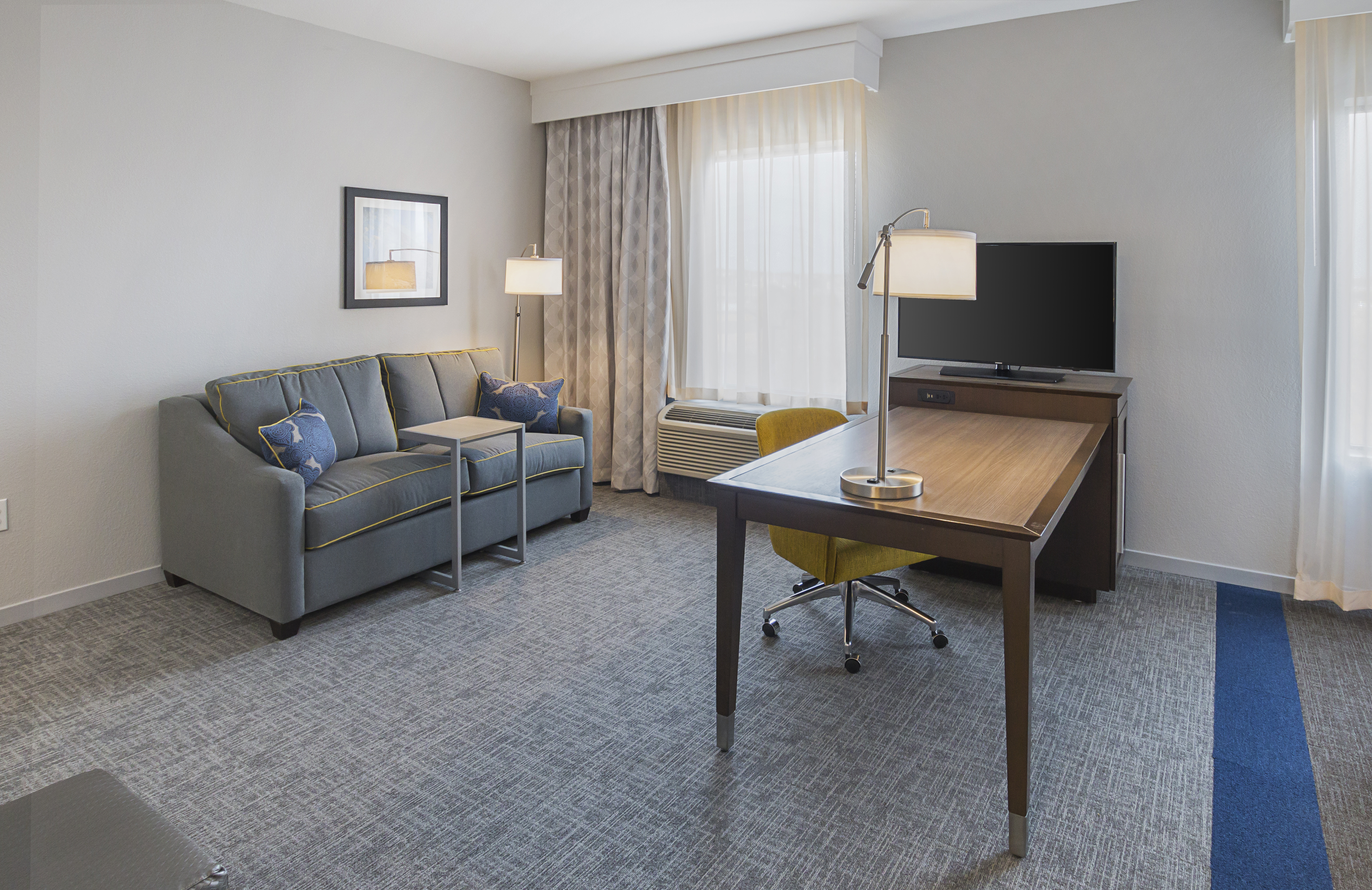 DFW hotel suite sofa bed, desk, desk
  chair, two lamps, and flat screen TV