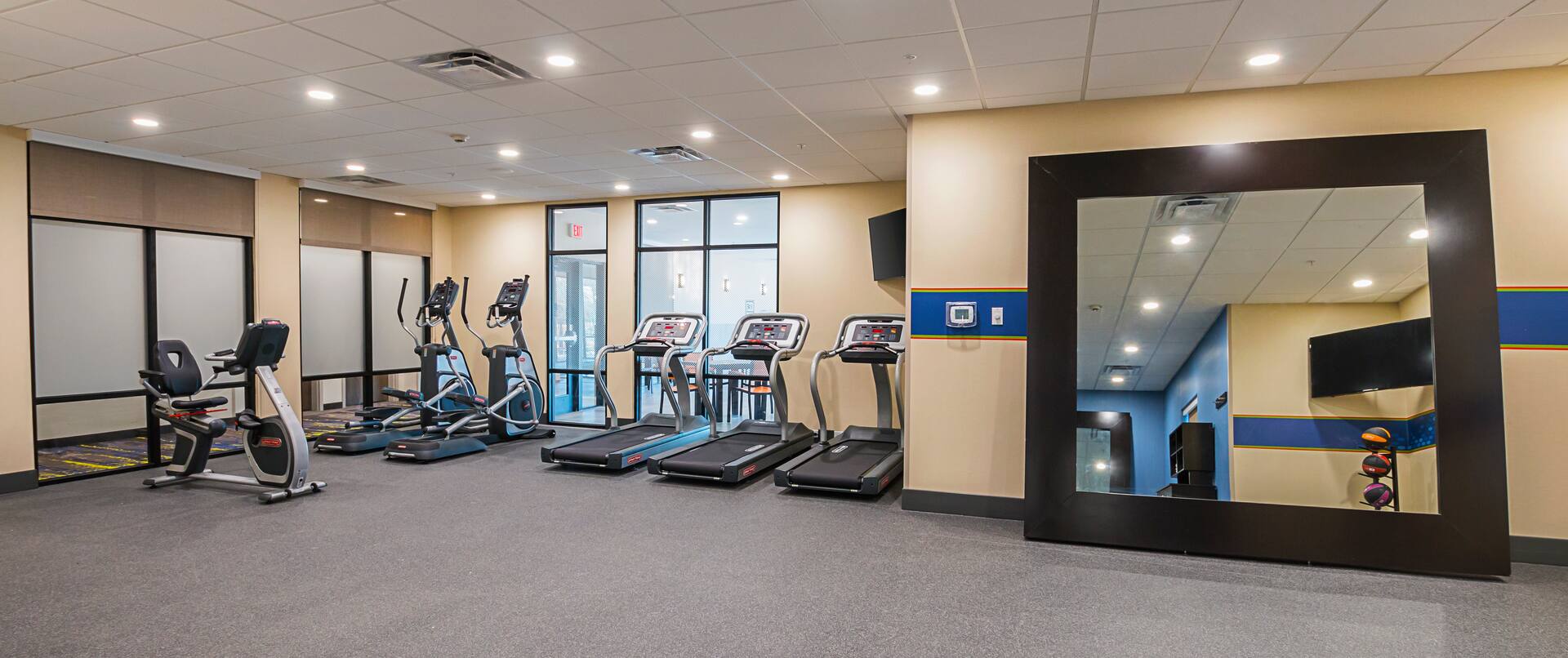 A well-lit hotel fitness center with
  treadmills, elliptical, and recumbent bike machines