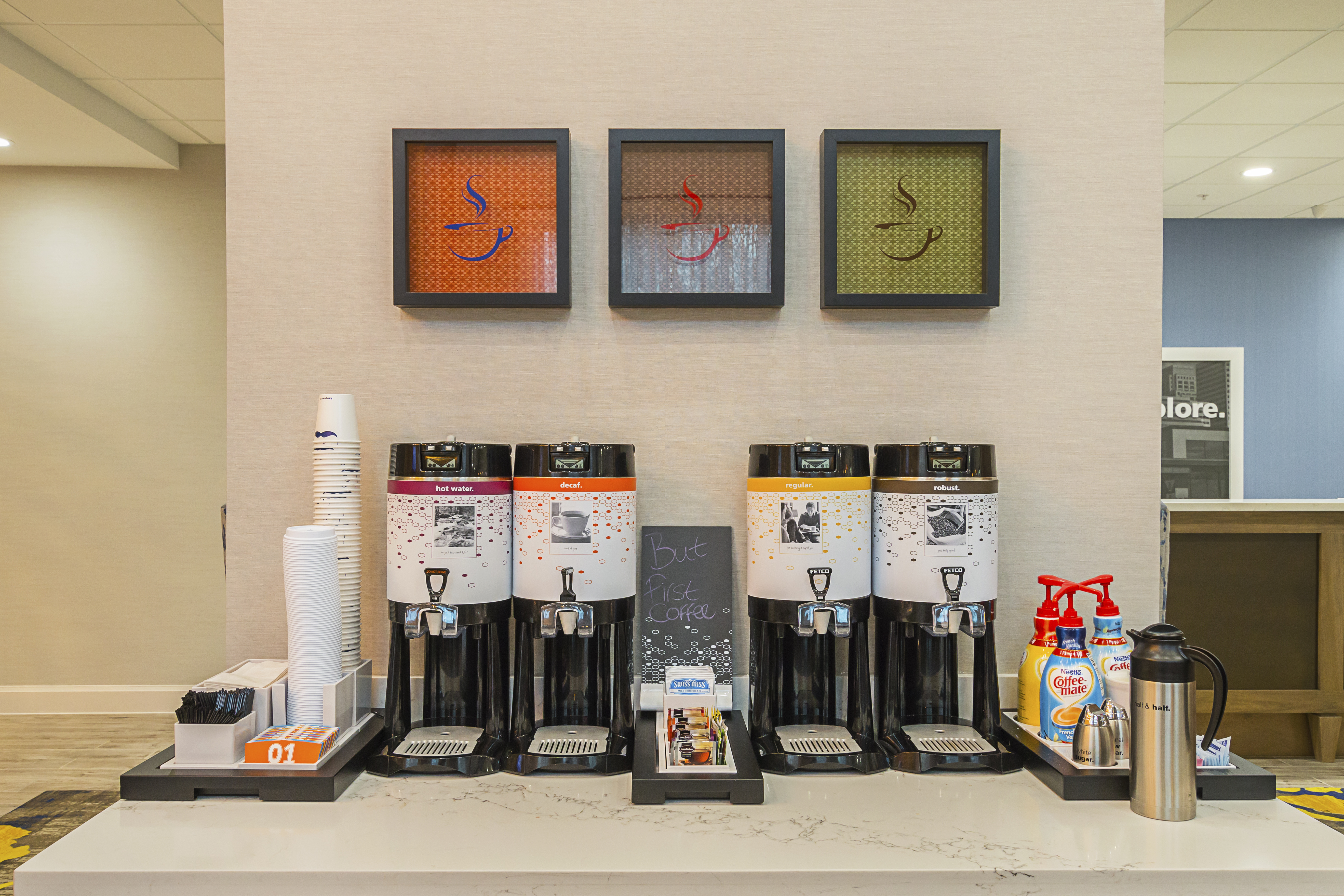 Hotel's free coffee and tea station with
  four hot beverage dispensers, creamer, and a variety of teas