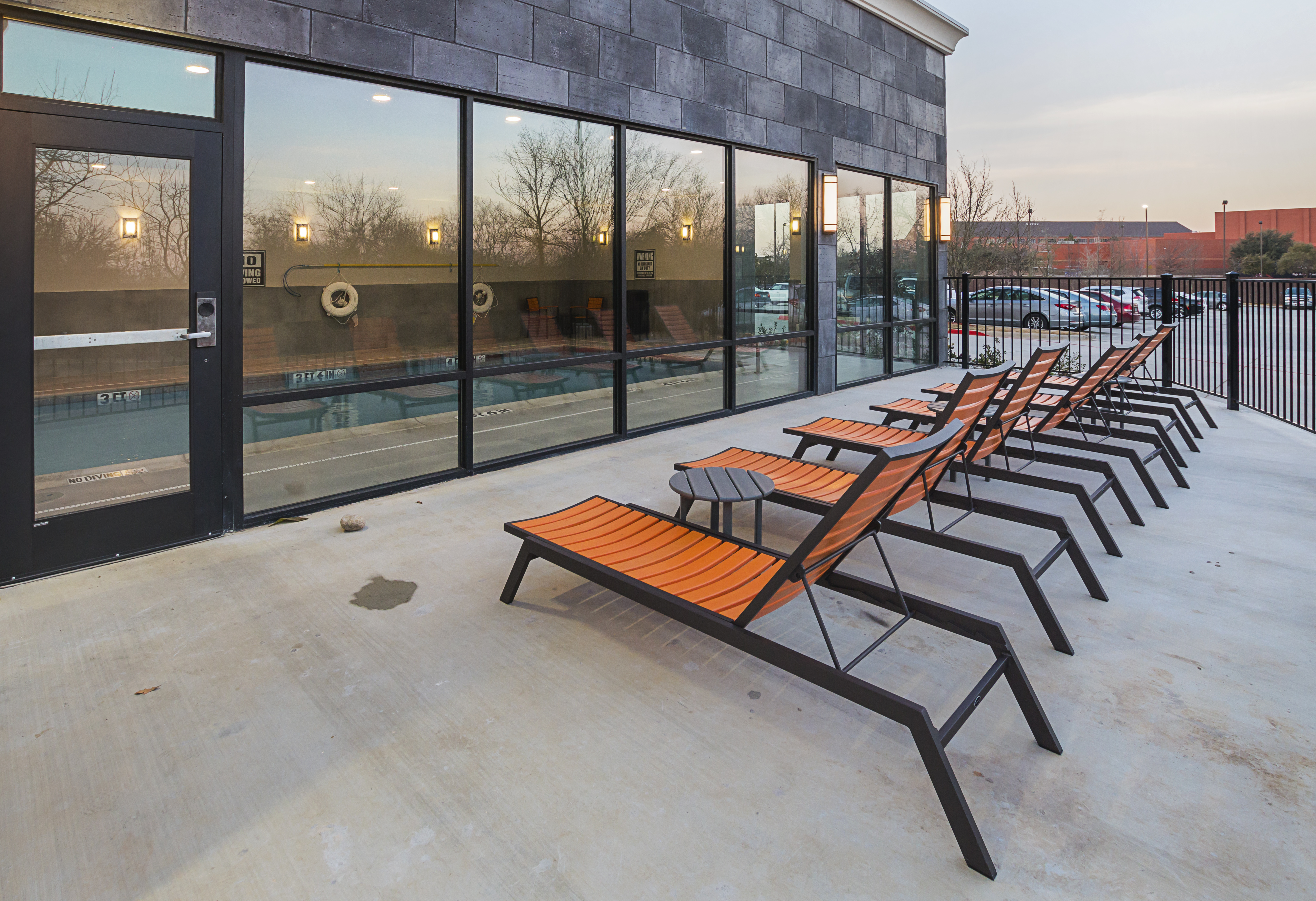Hotel patio with chaise lounge chairs and
  view of indoor pool through large windows and entry door