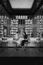 Man and woman sitting on bar stools facing each other as bar staff work in background