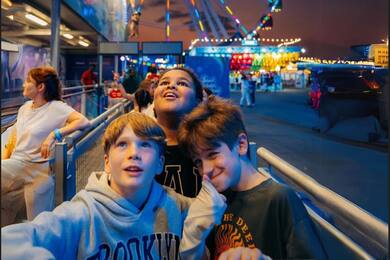 teen boys waiting in line for a ride, with a ferris wheel in the background.