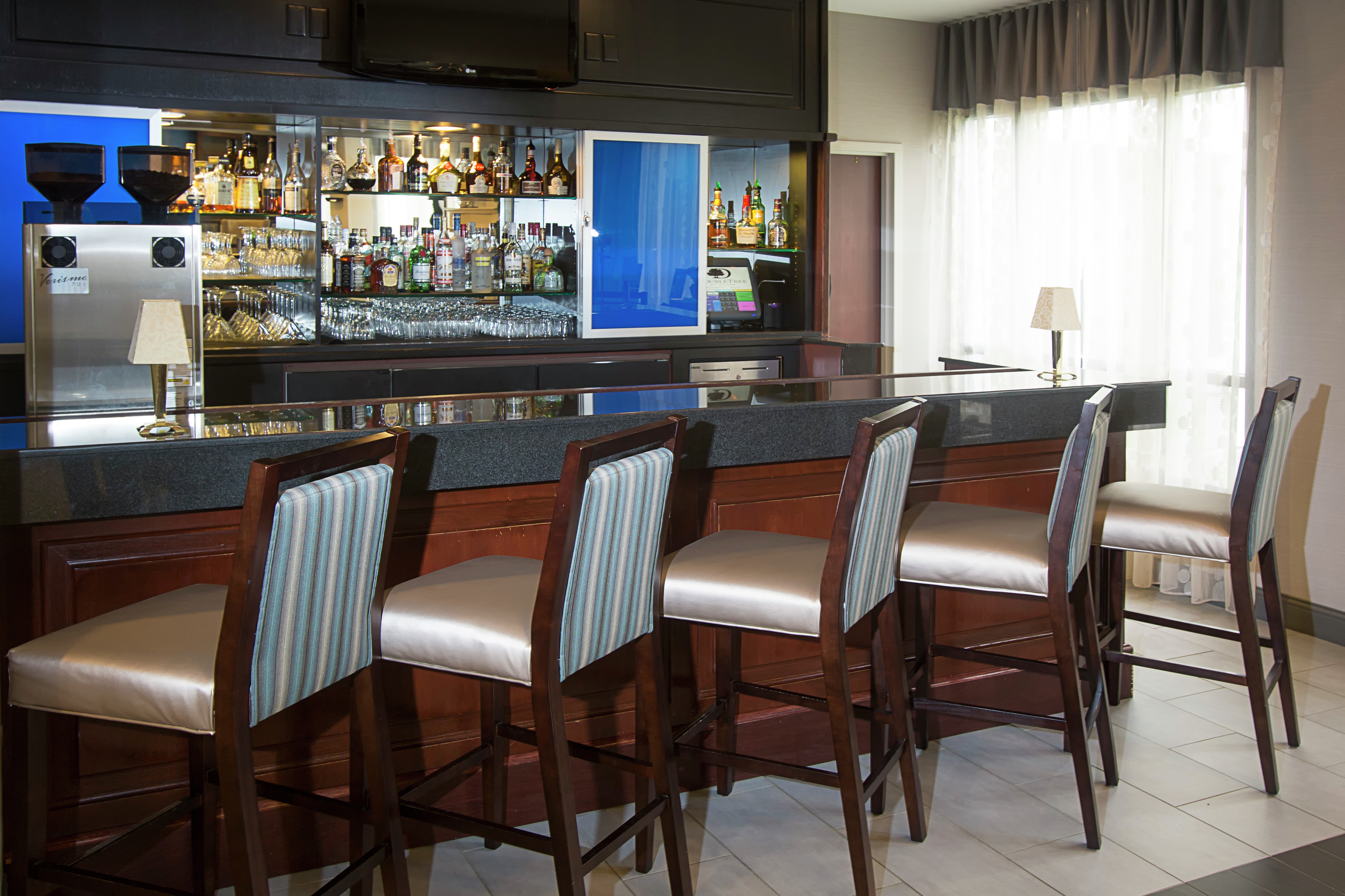 Bar stools in front of stylish bar with bottles and window in background