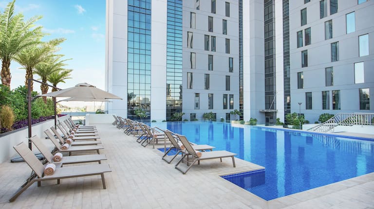 Outside View of Pool During the Day with Chaise Lounges Surrounding and Hotel In Background