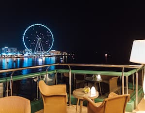 outdoor sky bar on patio with view of Ferris wheel and water at night