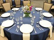 Detailed View of Place Settings, Flowers, White Napkins, and Candles on Round Tables With Blue Linens Surrounded by Tan Chairs for Banquet in Wilson Hall Meeting Space