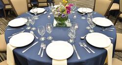 Detailed View of Place Settings, Flowers, White Napkins, and Candles on Round Tables With Blue Linens Surrounded by Tan Chairs for Banquet in Wilson Hall Meeting Space