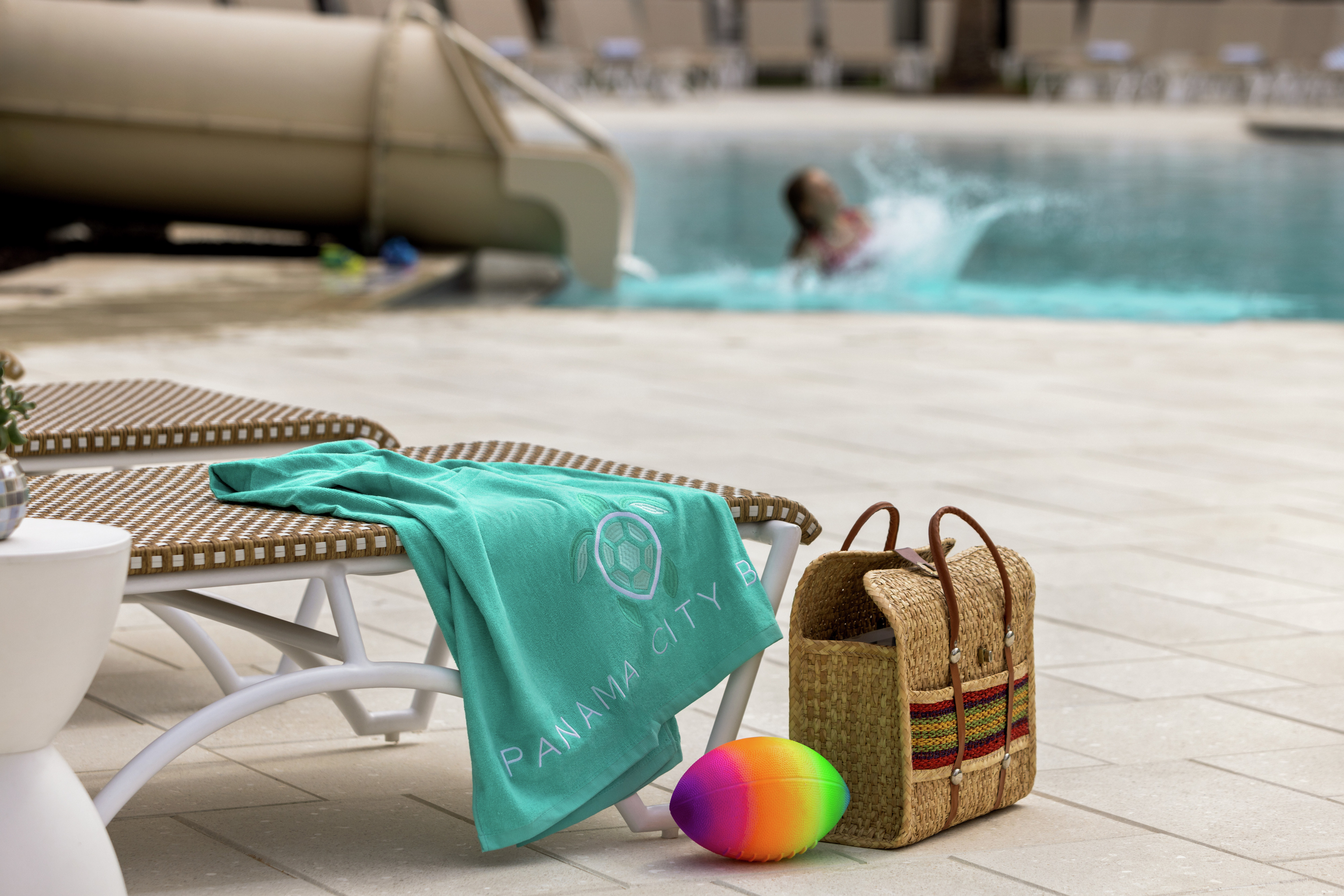 Detail of poolside accesories on lounge seating with a child enjoying the waterslide fun in the pool