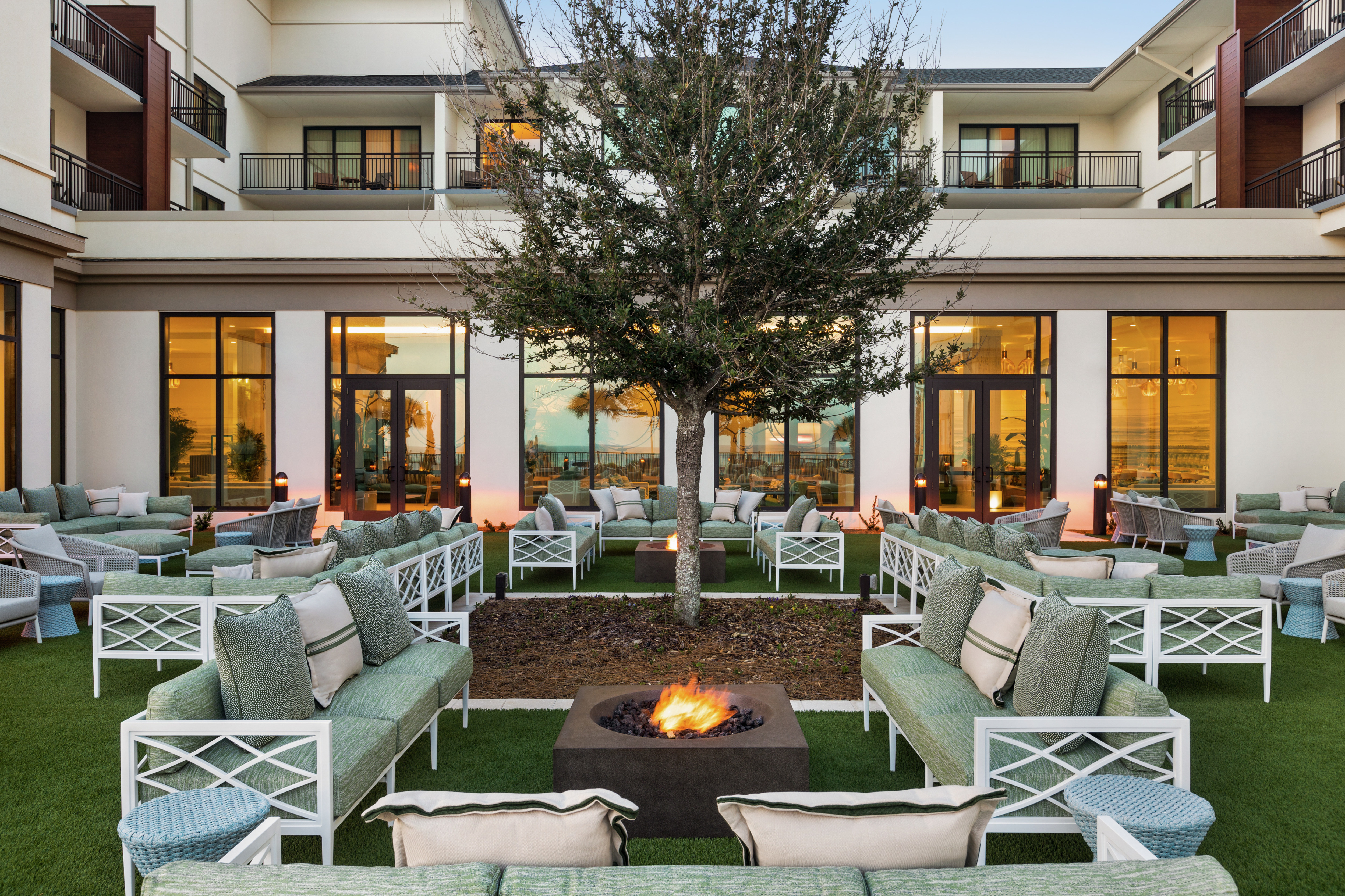 Outdoor courtyard fire pit at dusk surrounded by ample, sofa seating areas