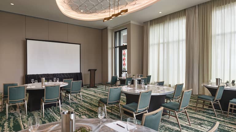 Spacious on-site meeting room with crescent rounds set up featuring large projector screen and podium 