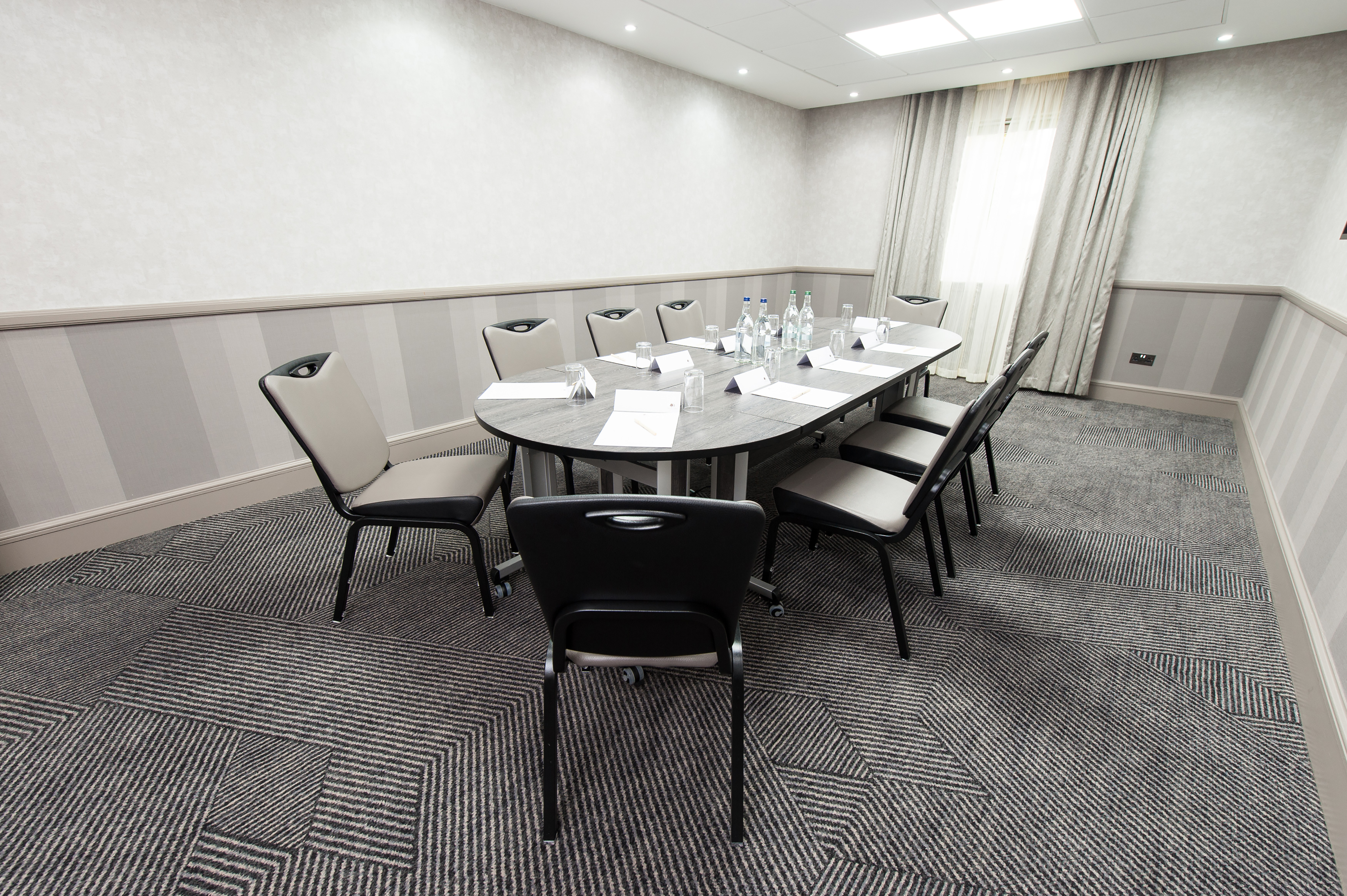 Meeting Room With Seating for Nine Around Boardroom Table With Water Bottles and Window With Long Drapes