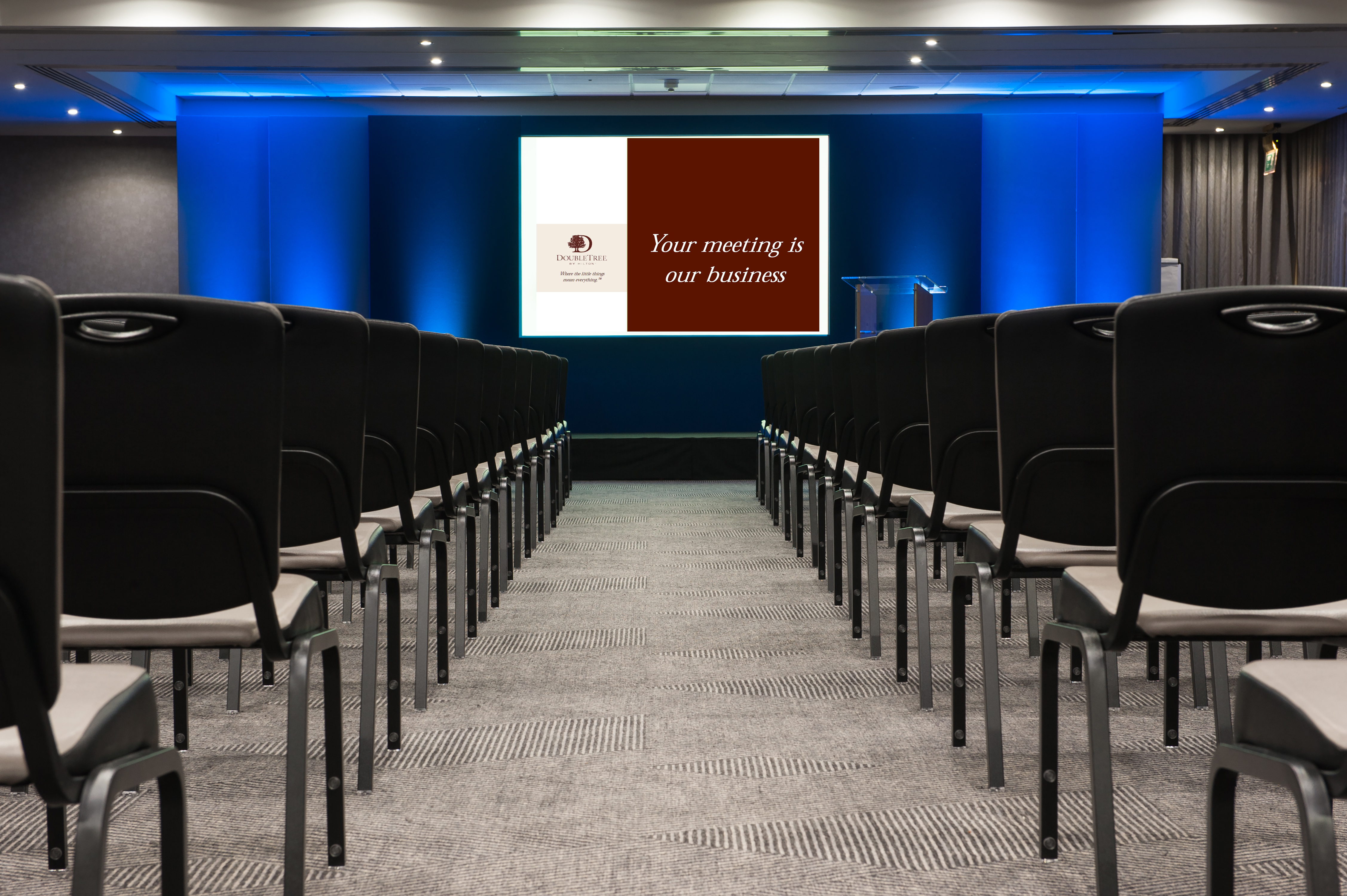 Meeting Room Arranged Theater Style With Rows of Black Chairs Facing Projector Screen and Podium