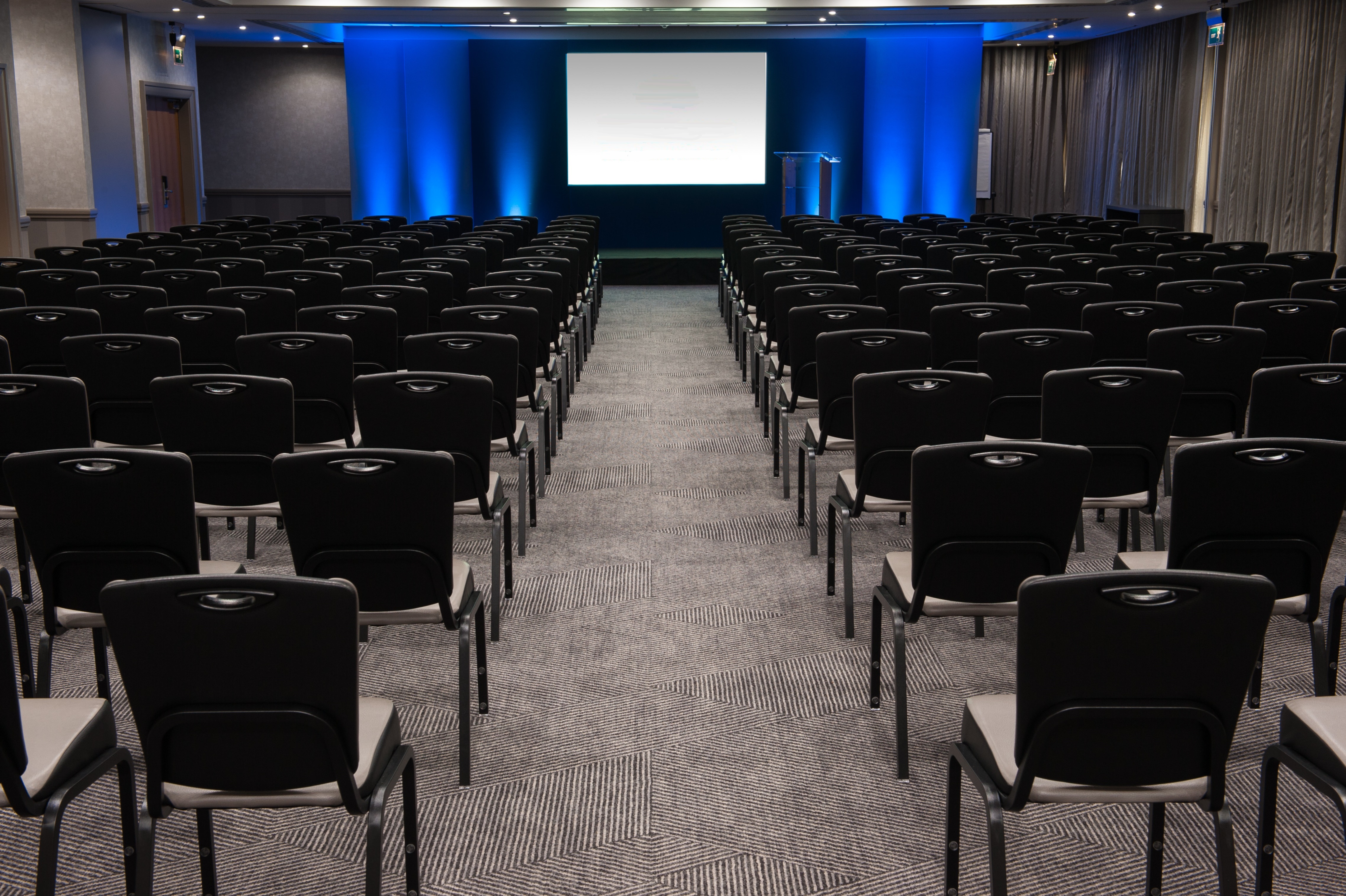 Edinburgh Suite Arranged Theater Style With Rows of Black Chairs Facing Dramatically Lit Projector Screen and Podium