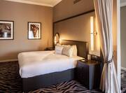 Wall Art, King Bed, Illuminated Lamps Above Bedside Tables With Connectivity Ports, and Partition Drape in Junior Suite