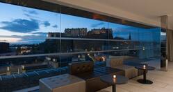 Tables With Illuminated Candles, and Lounge Seating by Large Window With View of Illuminated Castle at Dusk in SKYbar 