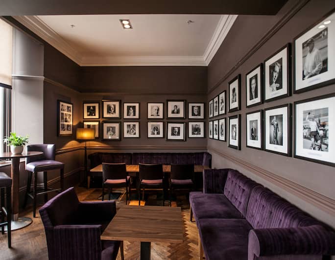 Window With Raised Shades, Purple Seating Options, Illuminated Lamps, and Wall Art in Cocktail Bar Lounge Area
