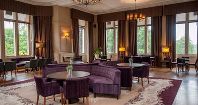Tables. Semicircle Sofas, Armchairs, Illuminated Lamps, and Large Windows With Open Drapes in Stuart Lounge