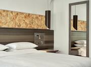 Neatly Made King, Reading Lamp on Headboard, Bedside Table and Full Length Mirror in Hotel Guest Room