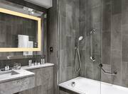Large Brightly Lit Vanity Mirror, Sink, Fresh Towels, Amenities, and Tub/Shower With Glass Doors in Standard Bathroom 