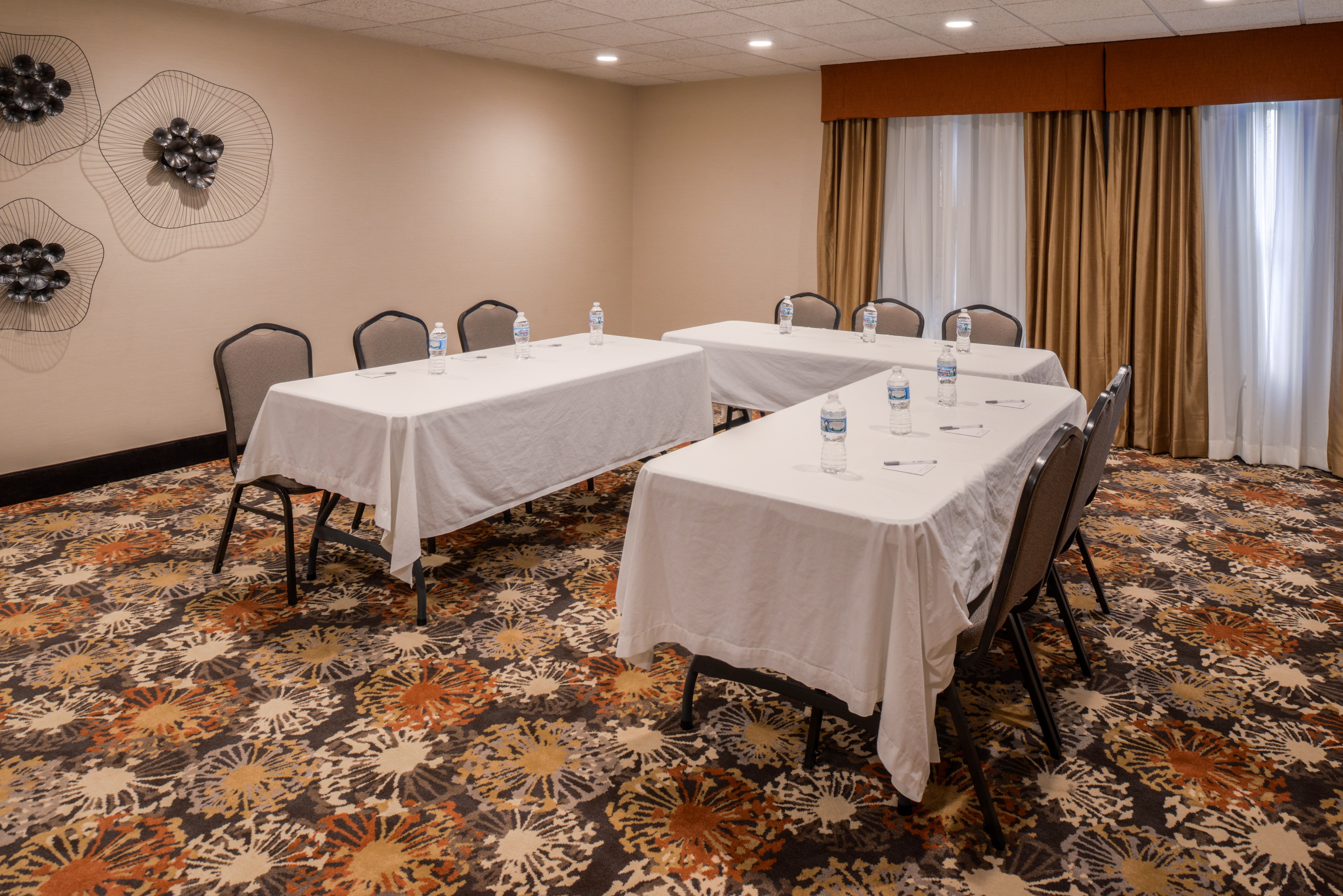 Three Left-Facing Tables with Tablecloths and Nine Chairs in Meeting Room Set Up in U-Shape