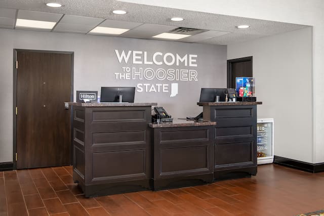 Hotel front desk reception area with two computers and white lettering on the wall behind it.