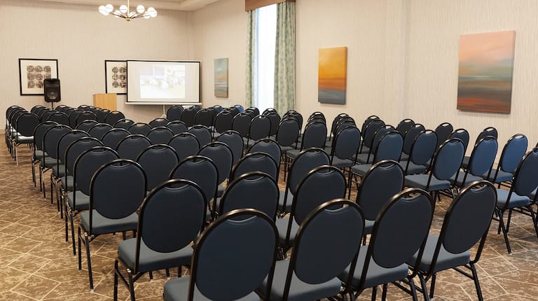 Meeting Room with Chairs in Theater Style Setup, Projector Screen, Floor Standing Speaker, and Lectern