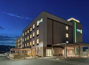  Modern Home2 Suites Hotel Exterior Featuring Glowing Guestroom Windows, Patio With String Lights, And Mountain View