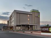 Modern Home2 Suites Hotel Exterior Featuring Outdoor Lounge With String Lights And Beautiful Dusk Sky