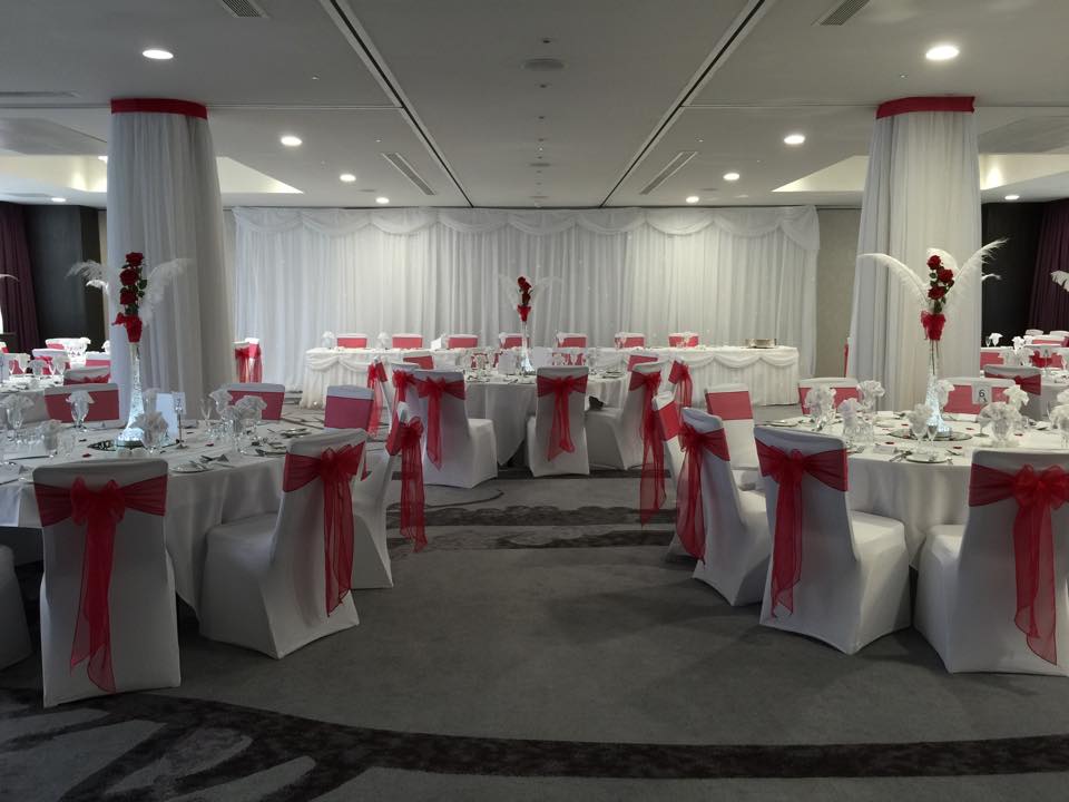 White Chairs With Red Bows, Head and Guest Tables With Place Settings and Red Roses, and White Feathers on White Linens in Orchard Suite Set Up for Wedding Breakfast