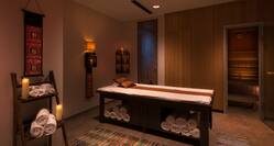 Dimly Lit Thai Massage Room With Candles, Rolled Towels, Table and Open Doorway to Sauna Area