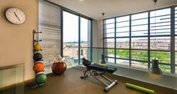 Fitness Center With Wall Clock, Weight Balls, Towels on Exercise Balls, Large Window With Open Blinds, Weight Bench, and Green Floor Mat