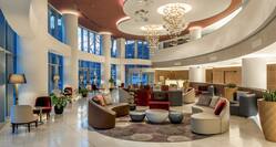 Tables, Chairs, Circle Seating, and Illuminated Floor Lamps in Lobby With Decorative Lighting, Large Windows, Entry, and View of Front Desk