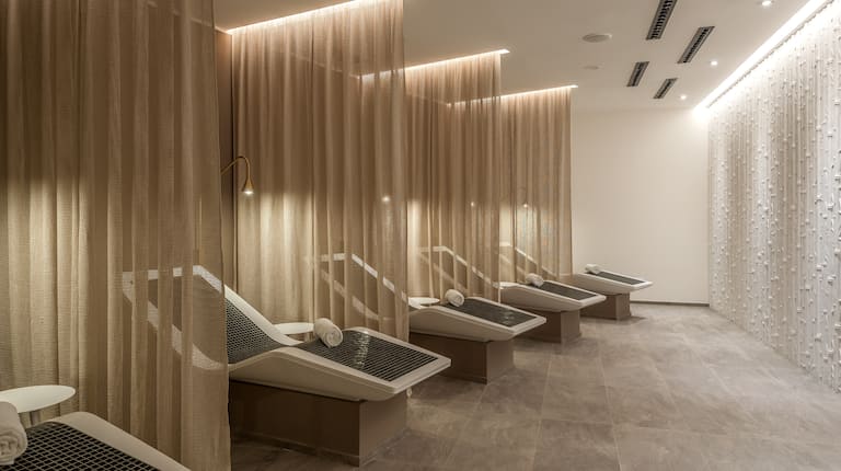 Five White Reclining Chairs With Fresh Towels Separated by Long Drapes in Atmosphere SPA