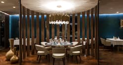 Circular Dining Area With Wood Partition, Seating For Six at Round Table Under Chandelier in Restaurant Gold