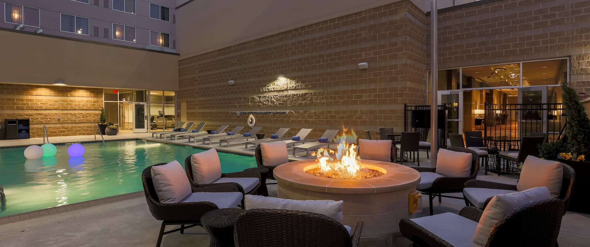 Loungers by Outdoor Pool and Soft Seating Around Fire Pit on Patio at Night