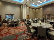 Round Dining Tables With Napkins and Flowers, Chairs, Podium and Entry Doors in Ballroom Set Up for Wedding Reception