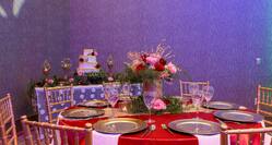 Chairs, Tables With Place Settings, White Napkins, and Flowers on Red Linens and Table With Candles and Wedding Cake in Ballroom Set Up for Wedding Reception