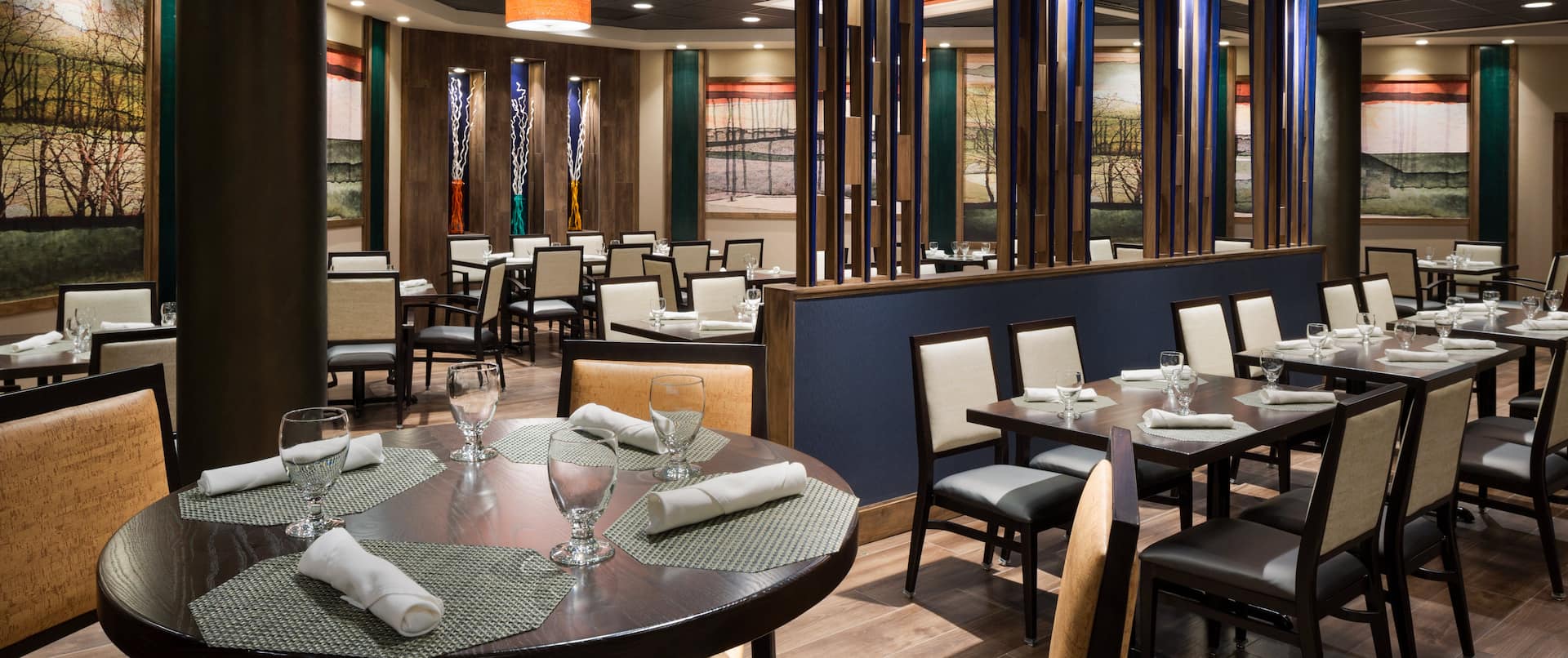 Windows, Wall Art, Chairs, and Mixed Tables With Place Settings in Dining Area of Seasonz Restaurant