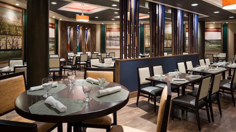 Windows, Wall Art, Chairs, and Mixed Tables With Place Settings in Dining Area of Seasonz Restaurant
