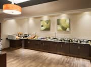 Wall Art Above Wood Cabinets With Hot and Cold Buffet Selections, Plates, Utensils, and Condiments on Counter in Breakfast Area