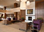 Tables, Soft Seating Around Fireplace, and Wall Art in Lobby Lounge Area With View of Check- in Desk 