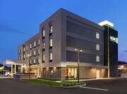 Modern Home2 Suites hotel exterior featuring porte cochere, glowing guestroom windows, and dusk sky.
