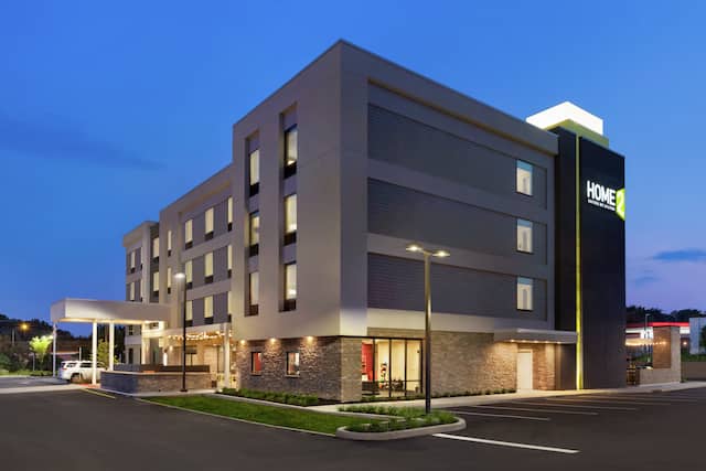 Modern Home2 Suites hotel exterior featuring porte cochere, glowing guestroom windows, and dusk sky.