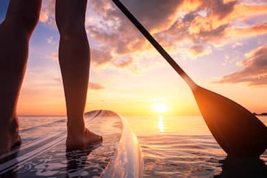 Closeup of a man's legs on a paddleboard with the sunset in the background