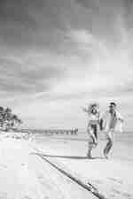 Pasangan Berjalan sembari Berpegang di Pantai