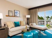 Suite Living Room With Wall Art, Lamps, Soft Seating, Table, Patio With Open Drapes and Pool View