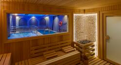 Wooden Sauna Interior With View of Hot Tub and Pool Through Large Window, Wood Benches, Heater and Bucket in Corner, and Entry